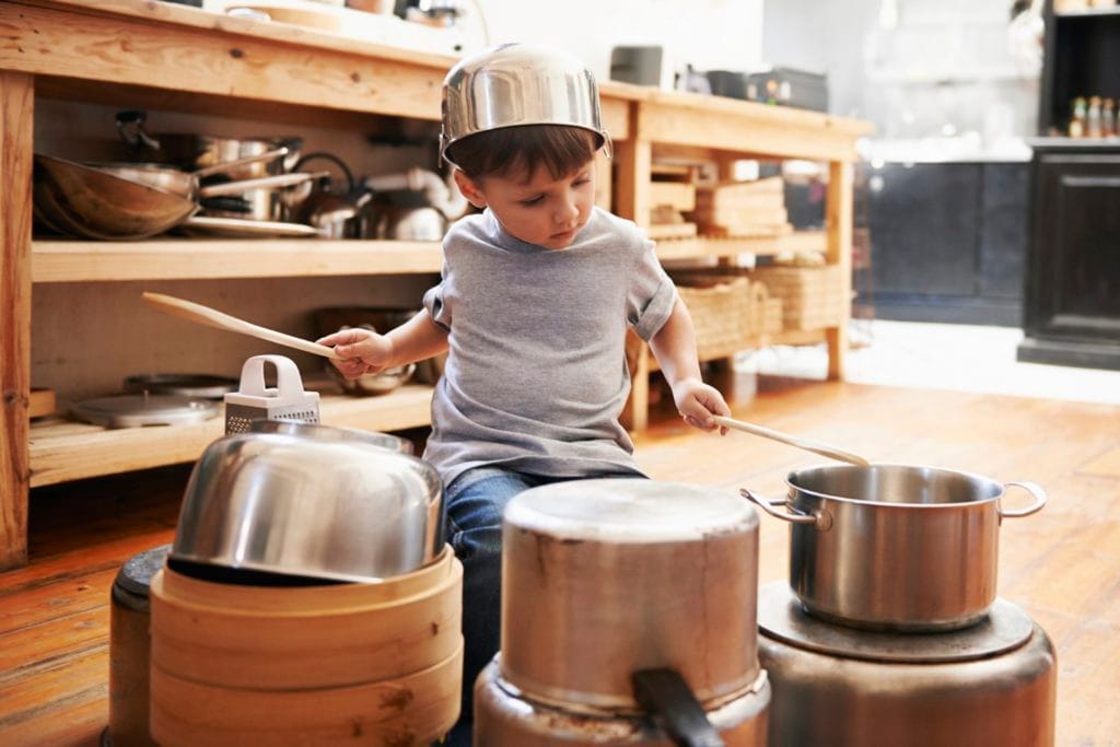 A young boy playing drums on pots and pans